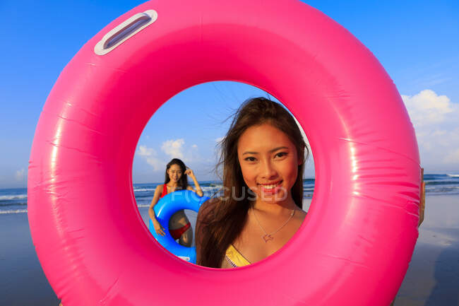 Dos jóvenes amigas asiáticas están jugando con sus flotadores en una playa en Bali. - foto de stock