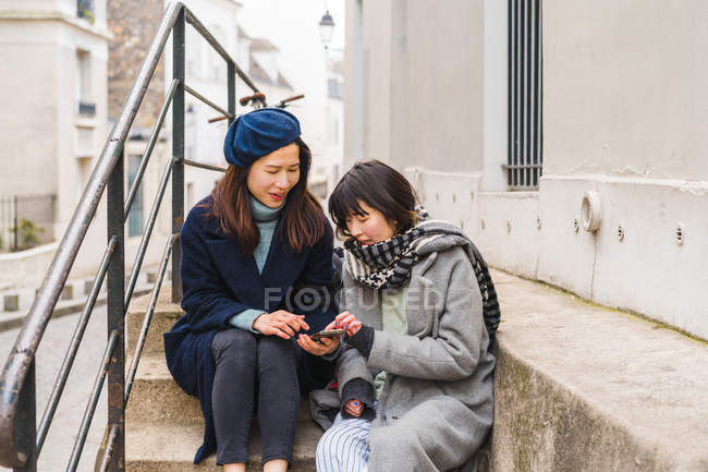 Young casual asian girls using smartphone in city — Stock Photo