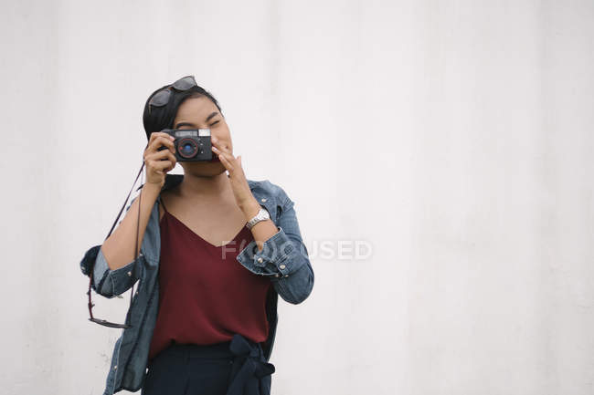 Jovem atraente asiático mulher tomando foto com câmera contra branco fundo — Fotografia de Stock