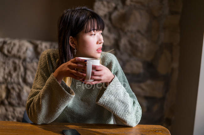 Young casual asian girl drinking coffee in cafe — Stock Photo