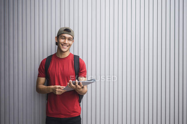Jovem asiático faculdade estudante com documentos posando contra cinza parede — Fotografia de Stock