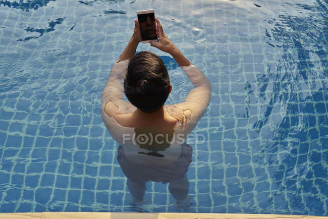 Jeune homme prenant des photos avec son téléphone portable dans la piscine — Photo de stock
