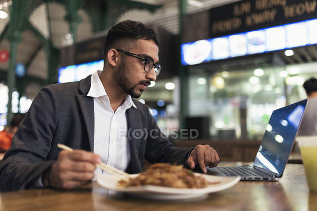 Bel homme d'affaires indien utilisant un ordinateur portable et manger dans un café — Photo de stock