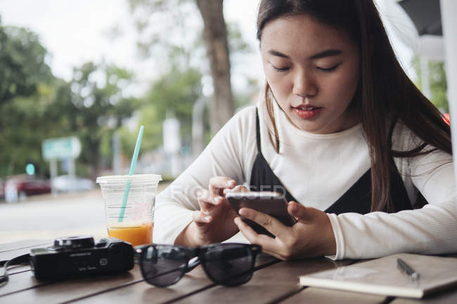 Mujer de pelo largo bastante chino usando teléfono inteligente en la cafetería - foto de stock