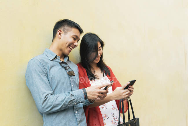 Young happy asian couple using smartphones together — Stock Photo