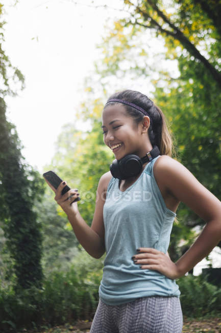 Jovem asiático mulher esportiva usando smartphone no parque — Fotografia de Stock