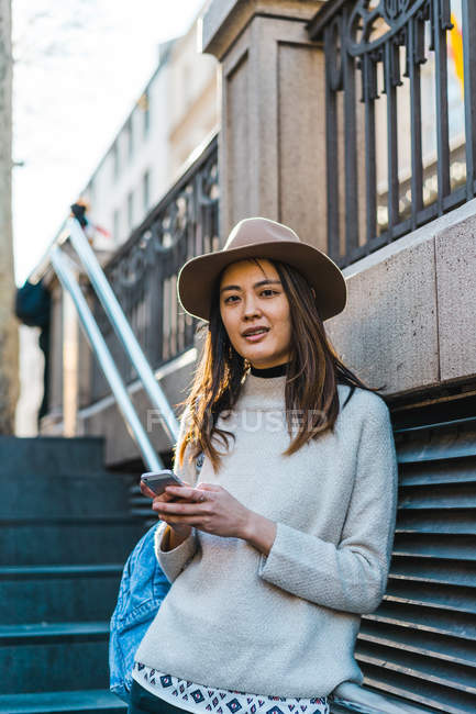 Jeune attrayant asiatique femme en utilisant smartphone sur escaliers — Photo de stock