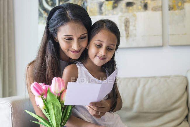 Young asian mother with cute daughter hugging at home with flowers and template — Stock Photo