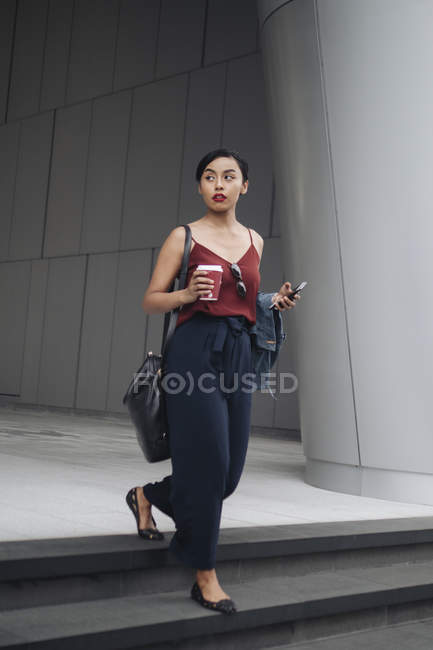 Young attractive asian woman having coffee and using smartphone outdoors — Stock Photo