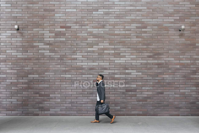 Handsome indian business man walking against brick wall — Stock Photo