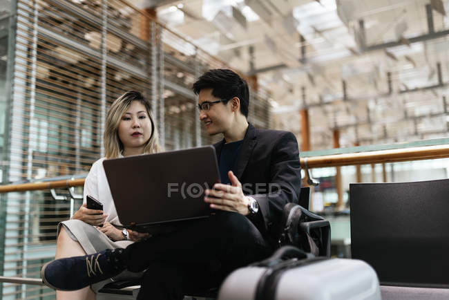 Успешная бизнес-азиатская пара вместе работает с ноутбуком в аэропорту — стоковое фото