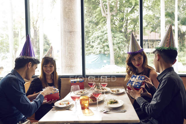 Щасливі молоді азіатські друзі святкують Різдво разом у кафе та діляться подарунками — стокове фото