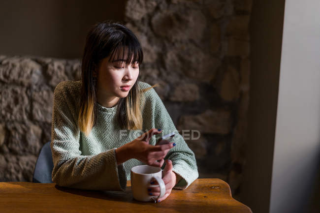 Jeune casual asiatique fille en utilisant smartphone dans café — Photo de stock