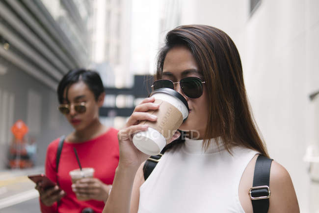 Young asian female friends together with coffee on city street — Stock Photo