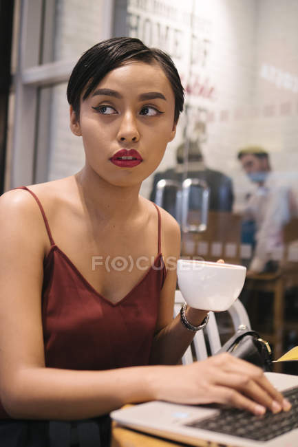 Молода приваблива азіатська жінка використовує ноутбук у кафе — стокове фото