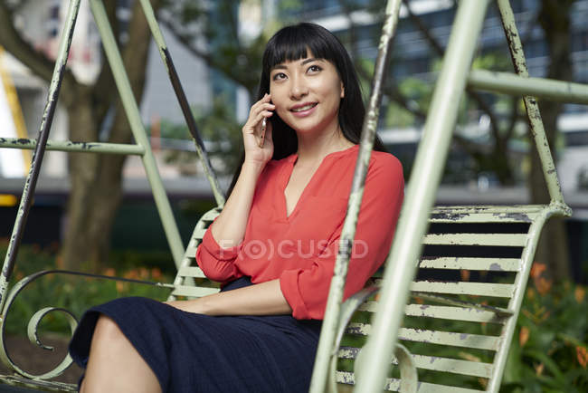 Junge attraktive asiatische Geschäftsfrau spricht auf der Schaukel auf dem Smartphone — Stockfoto