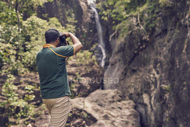 Vista trasera de un joven tomando fotos en la cascada de Klong Plu, Tailandia - foto de stock
