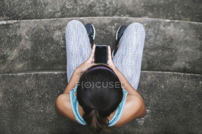 Jovem asiático mulher esportiva usando smartphone em escadas — Fotografia de Stock
