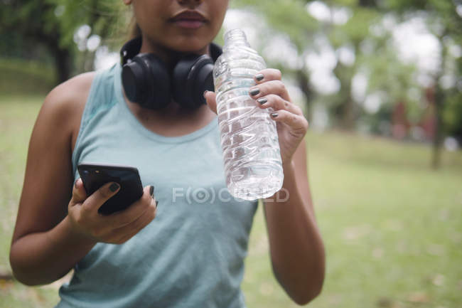 Joven asiático deportivo mujer beber agua y usando smartphone - foto de stock