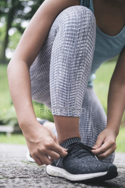 Imagen recortada de mujer joven deportiva atando cordones de zapatos - foto de stock