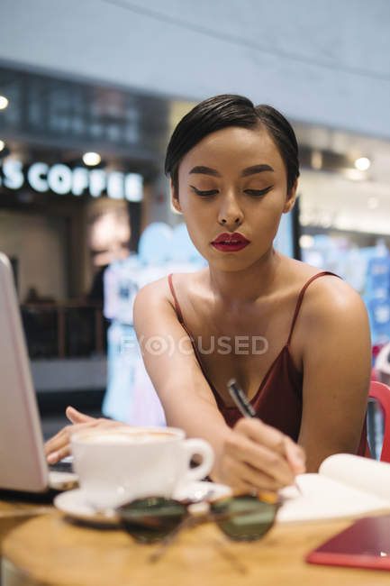 Молода приваблива азіатська жінка пише нотатки в кафе — стокове фото