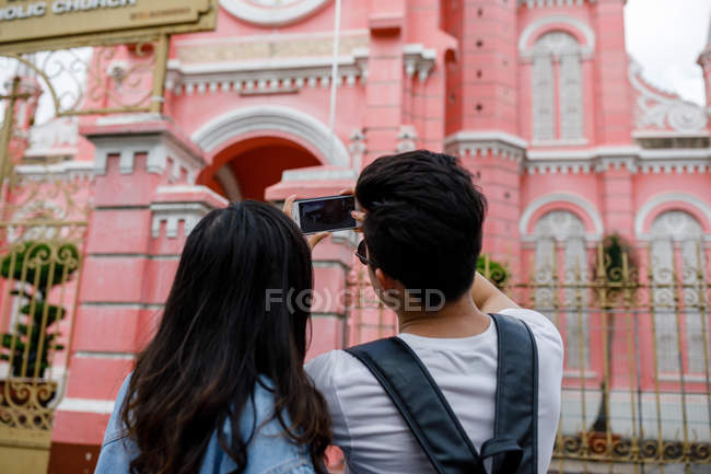 Joven pareja asiática tomando fotos de la catedral, Ho Chi Minh City, Vietnam - foto de stock