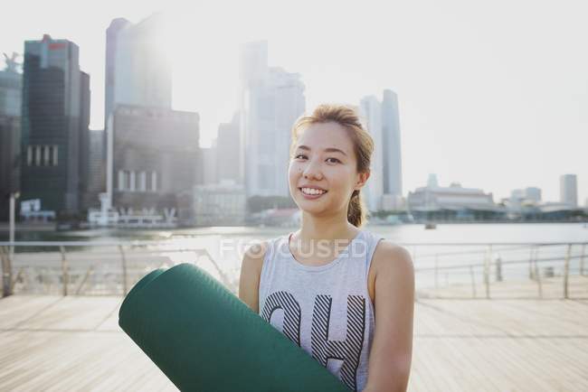 Young sporty asian woman with yoga mat at pier — Stock Photo