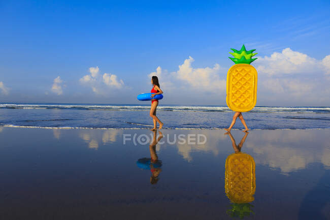 Two pretty girls with floaties on the way to the waves of the ocean. — Stock Photo