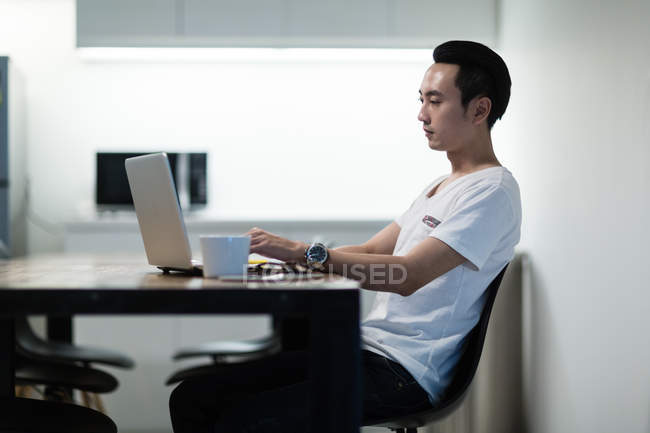 Jeune homme asiatique travaillant dans le bureau moderne avec ordinateur portable — Photo de stock