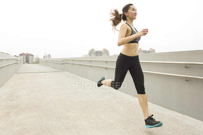 A young asian, female runner is running down a ramp in Singapore. — Stock Photo