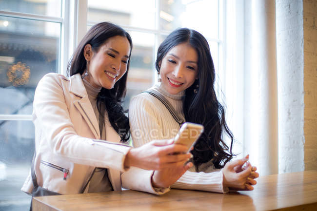 Дві красиві азіатські жінки використовують смартфон разом — стокове фото