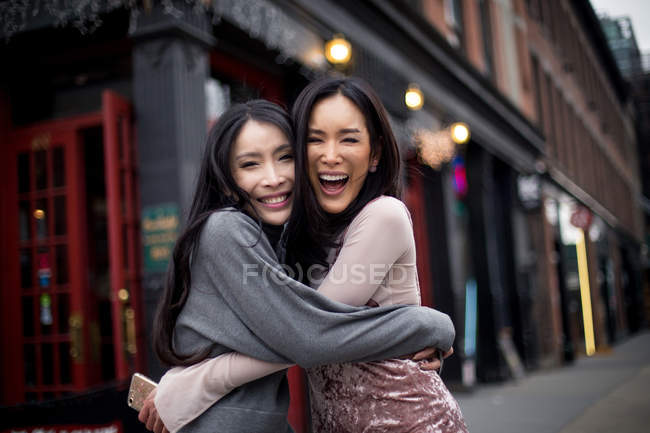 Two asian girl friends hugging on city street — Stock Photo