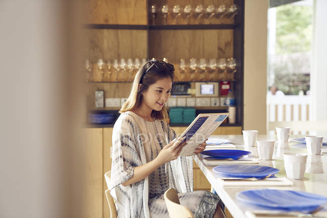 Jeune jolie asiatique femme regardant menu dans café — Photo de stock