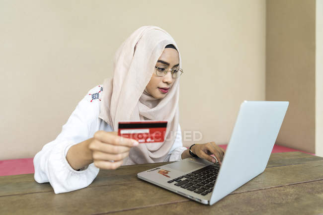 Giovane asiatica musulmana donna utilizzando laptop e in possesso di carta di credito — Foto stock