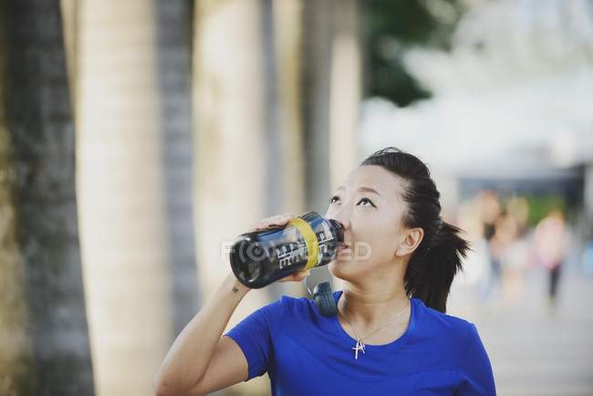 Молода азіатська спортивна жінка п'є воду з пляшки — стокове фото