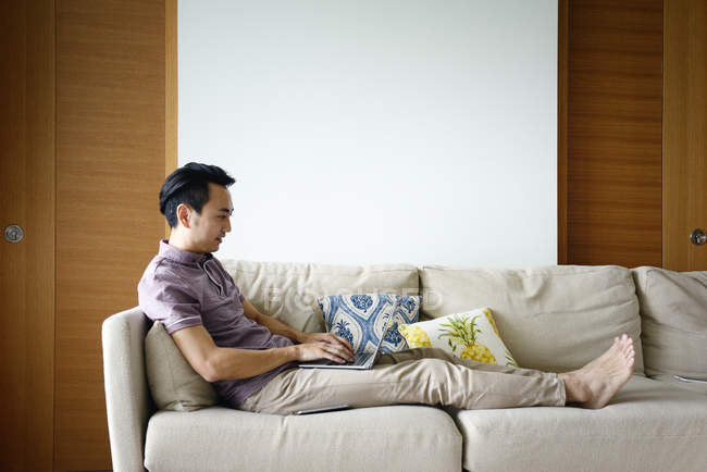 Vue latérale de l'homme asiatique adulte en utilisant un ordinateur portable à la maison — Photo de stock