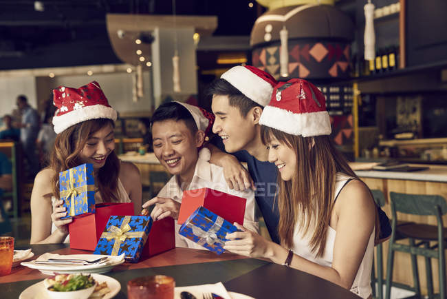 Счастливые молодые люди и их друзья вместе празднуют Новый год в кафе и делятся подарками — стоковое фото
