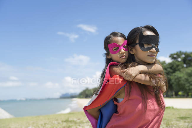 Молодая азиатская мать с симпатичной дочерью в костюмах супергероя позирует на фоне голубого неба — стоковое фото