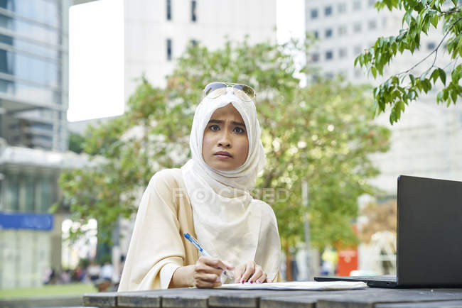 Young Malay woman in a Tudung signing documents in frustration — Stock Photo