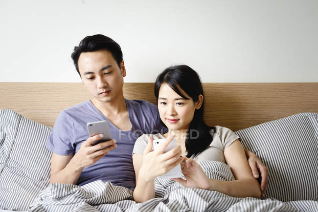 Adulto asiatico coppia insieme utilizzando smartphones a casa — Foto stock