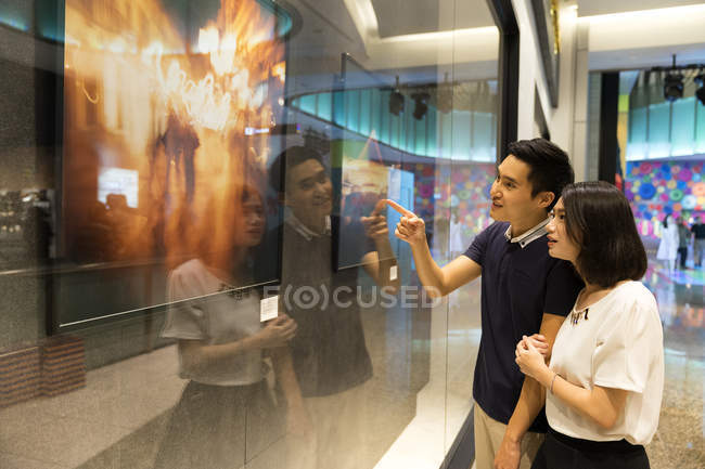 Jovem atraente asiático casal juntos compras e olhando no tv tela — Fotografia de Stock