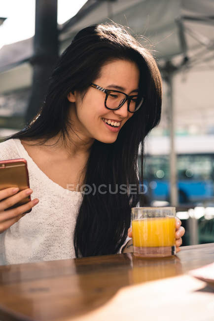 Китайская девушка с телефоном и пьющая апельсиновый сок на террасе Мадрида, Испания — стоковое фото