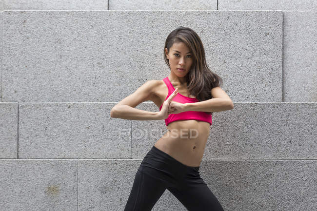 A young asian woman in power fitness poses in front of a concrete wall. — Stock Photo