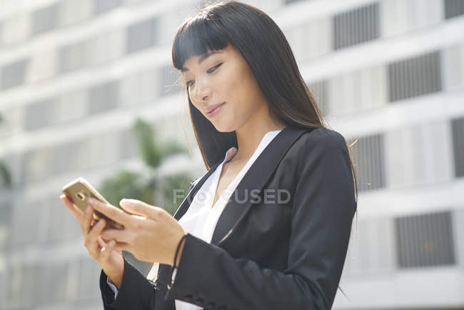 Young attractive asian businesswoman using smartphone in city — Stock Photo