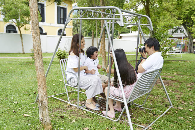 Happy young asian family together taking photo on bench — Stock Photo