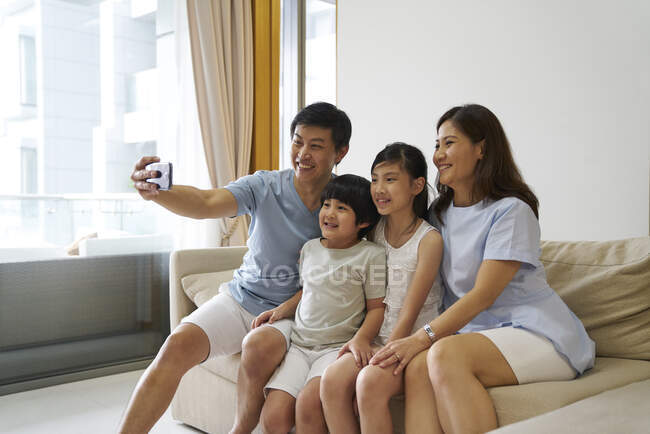 Felice giovane famiglia asiatica insieme prendendo selfie a casa — Foto stock