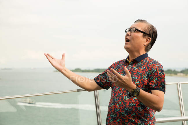 Elderly man sings on a balcony with a sea view — Stock Photo