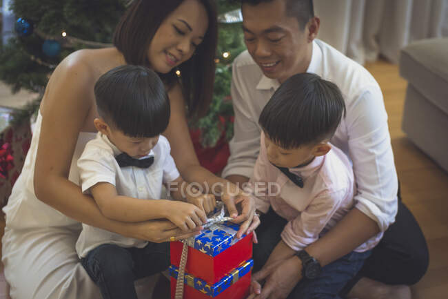 Mother and father and their two sons sit together on the floor and they prepare a few Christmas presents for friends. — Stock Photo