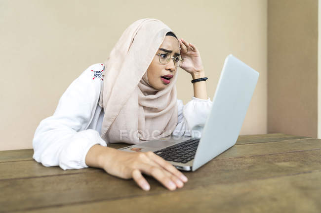 Молода напружена мусульманка використовує ноутбук у приміщенні — стокове фото