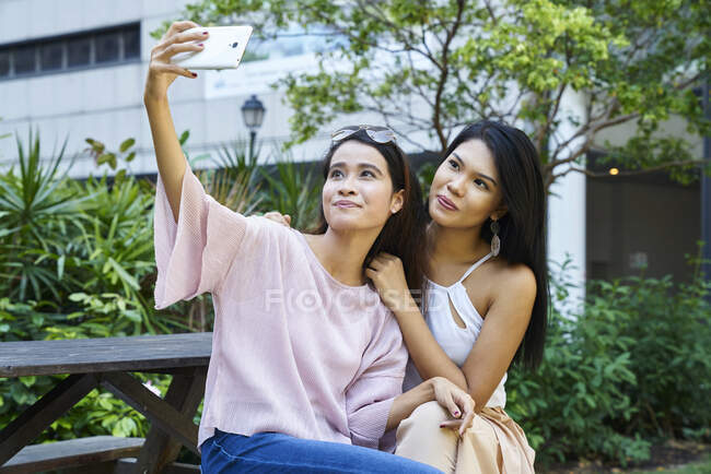Junge malaiische Frauen machen ein Selfie auf einer Holzbank — Stockfoto